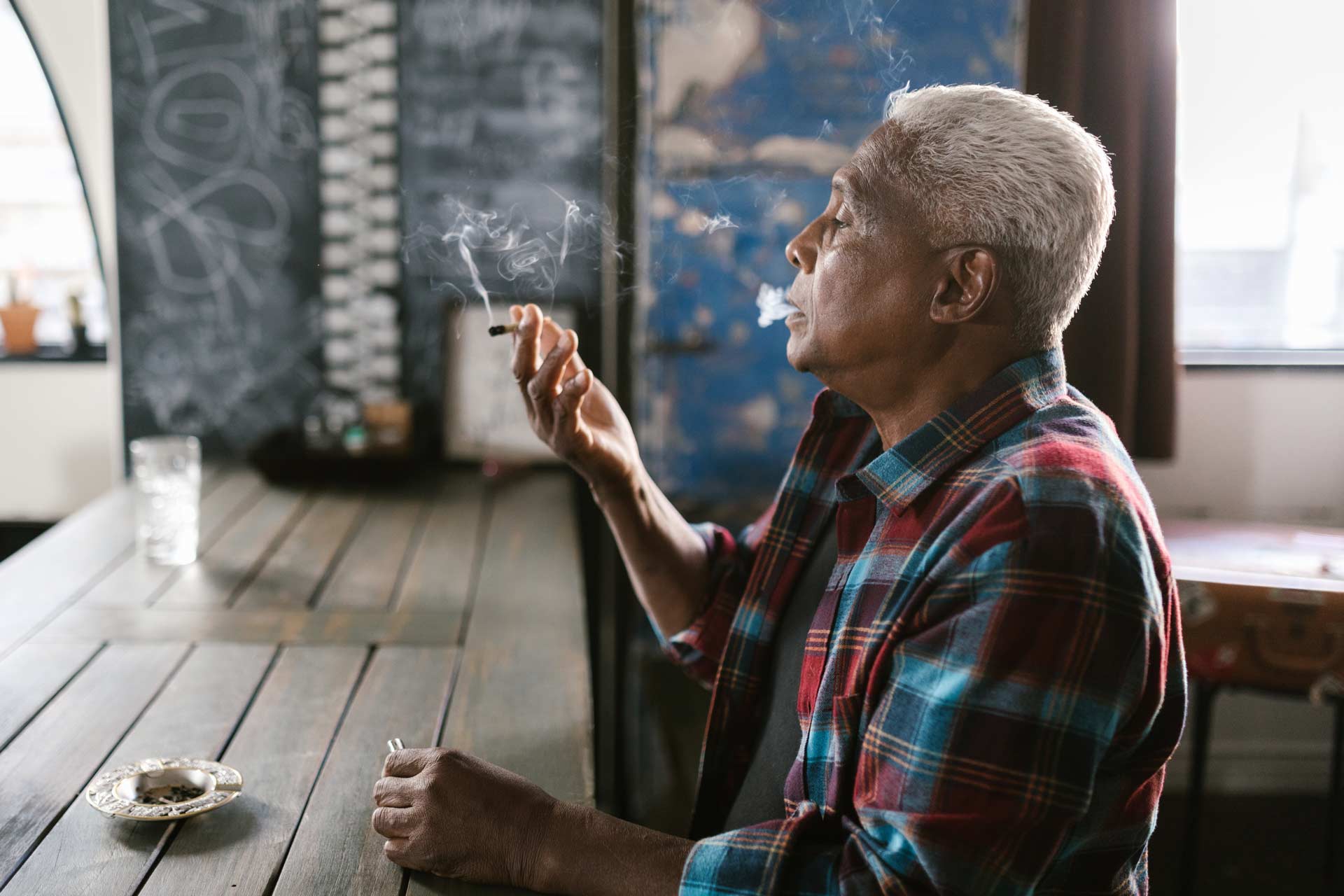 older man sits at table and smokes a joint